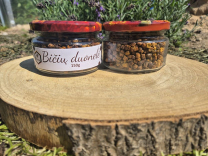 Ant kelmo pastatyti 150g. Bičių duonelės stiklainiukai, šone stovi levandų krūmelis.