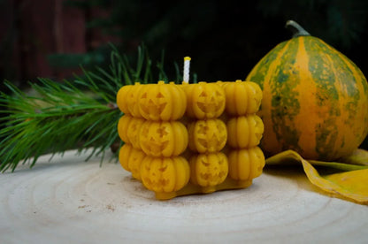 Melora natūralaus bičių vaško kubo formos žvakė sudaryta iš daug mažų kubelių ir kampu pastatyta ant medinio kelmo.